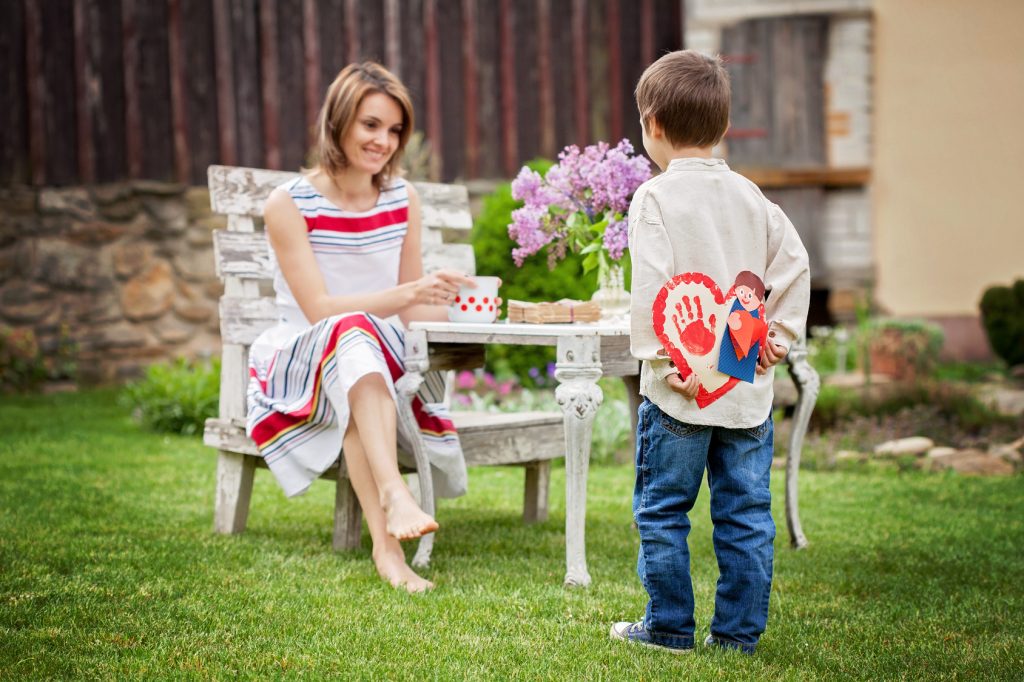 Beautiful mom, having coffee in a backyard, young cute child giv